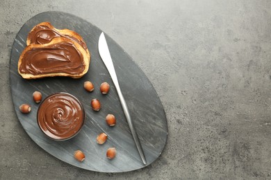 Photo of Toasts with tasty chocolate spread and hazelnuts on gray textured table, top view. Space for text