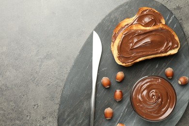 Photo of Toasts with tasty chocolate spread and hazelnuts on gray textured table, top view. Space for text