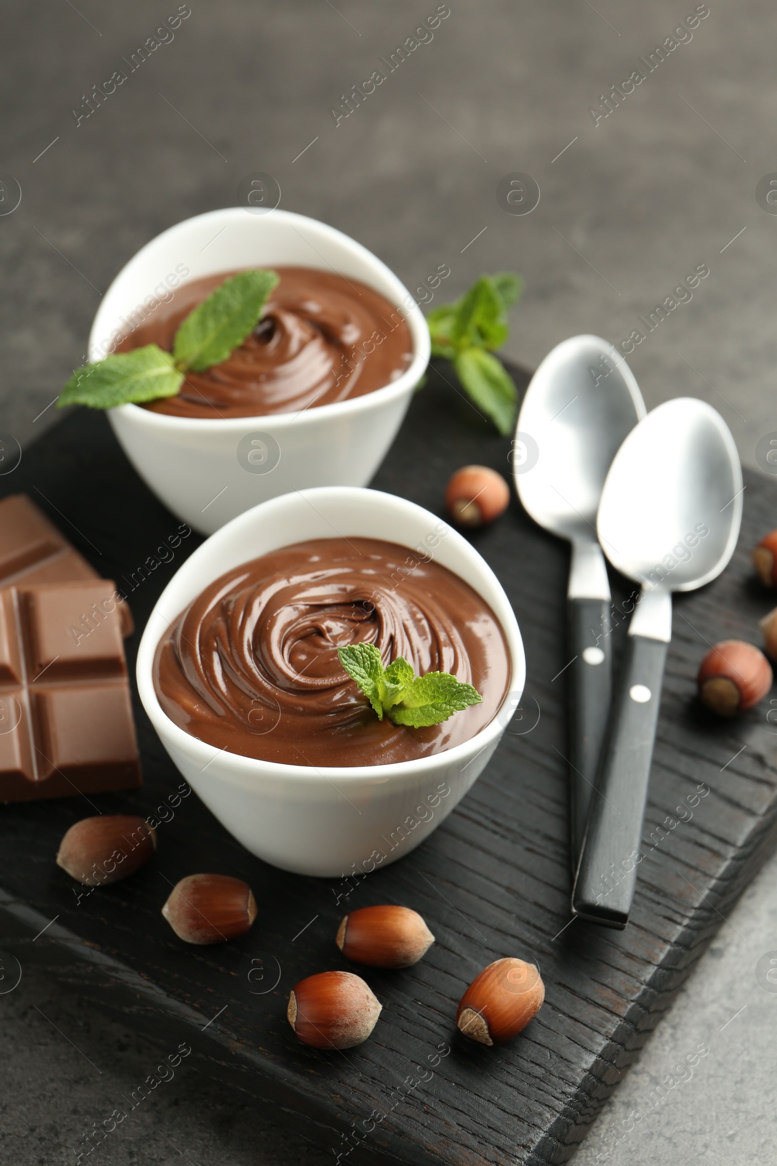 Photo of Tasty chocolate spread, pieces, mint and hazelnuts on gray table, closeup