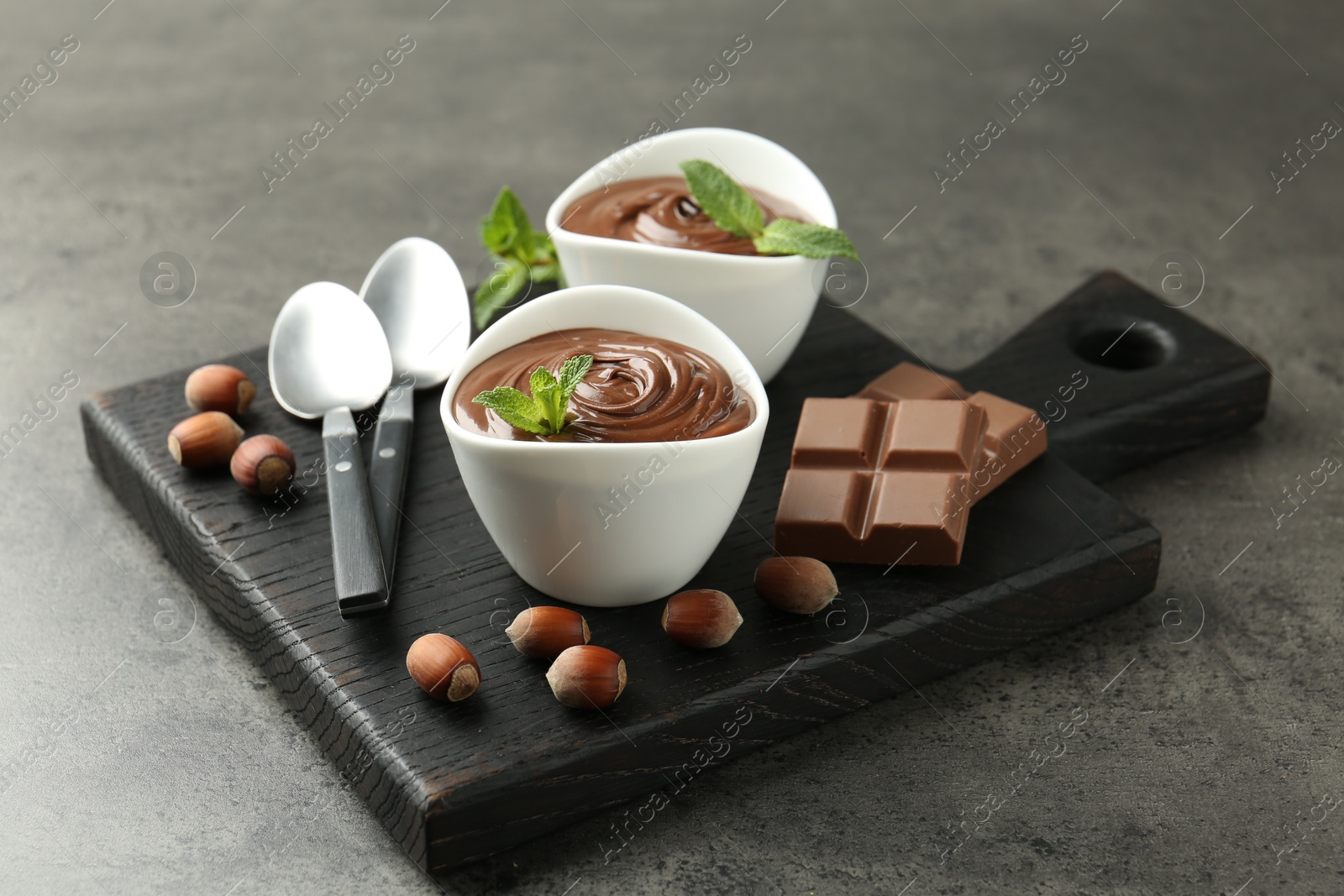 Photo of Tasty chocolate spread, pieces, mint and hazelnuts on gray textured table, closeup