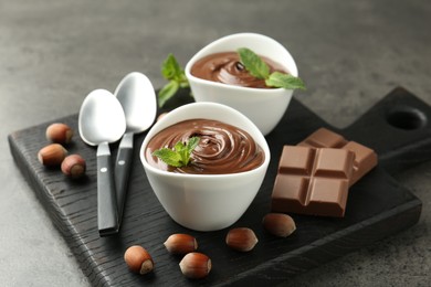 Photo of Tasty chocolate spread, pieces, mint and hazelnuts on gray textured table, closeup