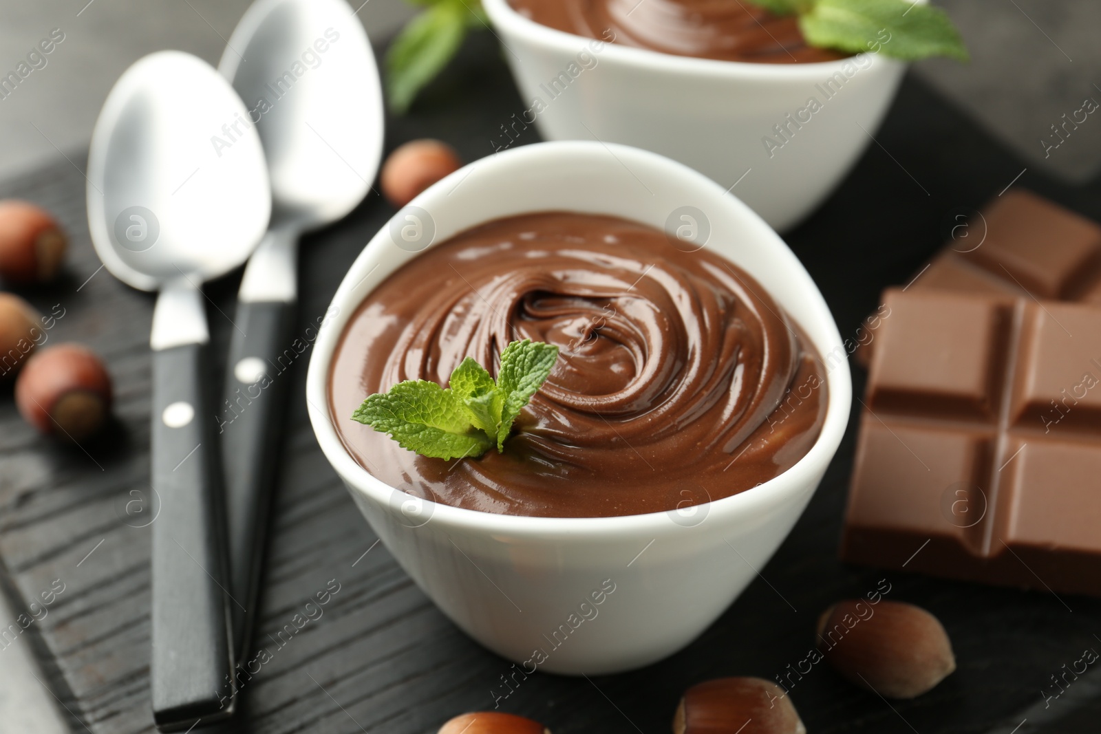 Photo of Tasty chocolate spread, pieces, mint and hazelnuts on table, closeup