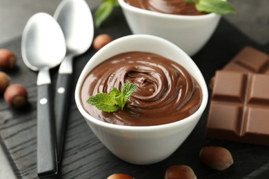 Photo of Tasty chocolate spread, pieces, mint and hazelnuts on table, closeup