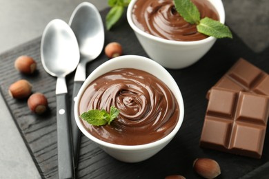 Photo of Tasty chocolate spread, pieces, mint and hazelnuts on table, closeup