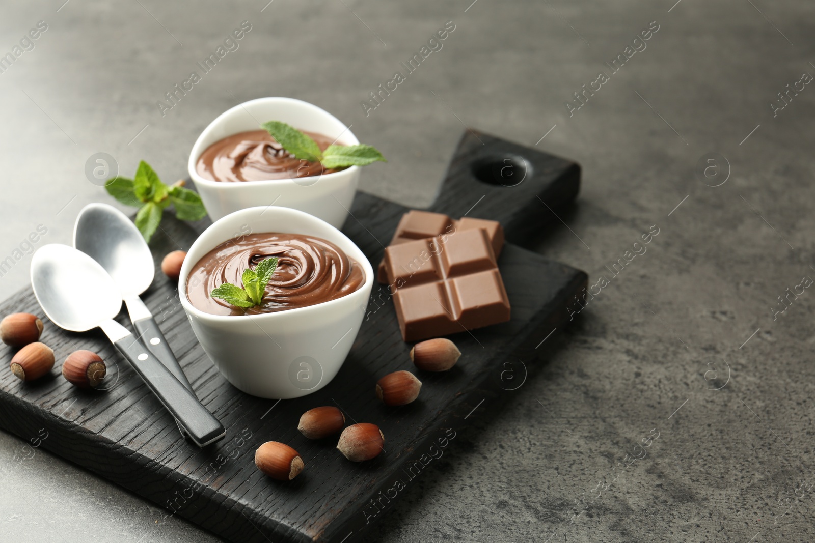 Photo of Tasty chocolate spread, pieces, mint and hazelnuts on gray textured table, closeup