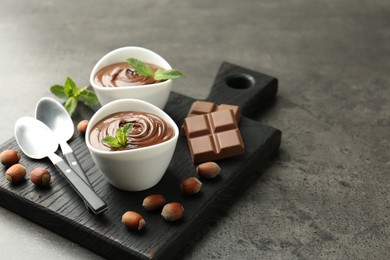 Photo of Tasty chocolate spread, pieces, mint and hazelnuts on gray textured table, closeup