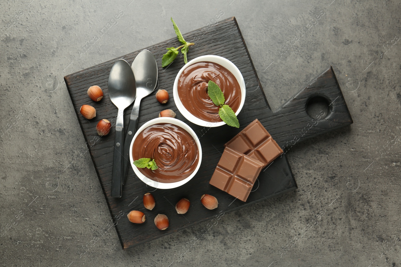 Photo of Tasty chocolate spread, pieces, mint and hazelnuts on gray textured table, top view
