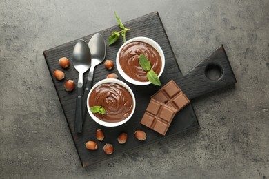Photo of Tasty chocolate spread, pieces, mint and hazelnuts on gray textured table, top view