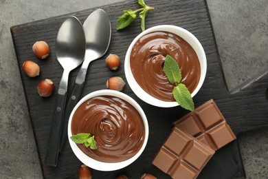 Photo of Tasty chocolate spread, pieces, mint and hazelnuts on gray textured table, top view