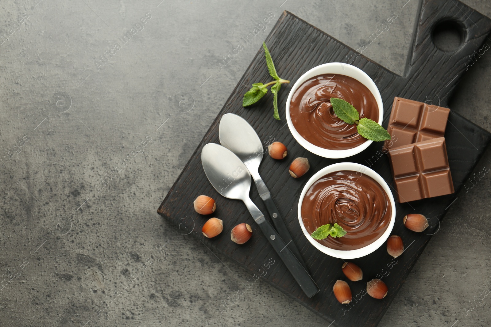 Photo of Tasty chocolate spread, pieces, mint and hazelnuts on gray textured table, top view. Space for text
