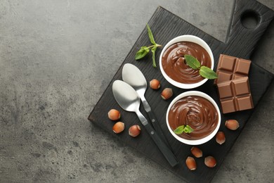 Photo of Tasty chocolate spread, pieces, mint and hazelnuts on gray textured table, top view. Space for text