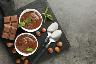 Photo of Tasty chocolate spread, pieces, mint and hazelnuts on gray textured table, top view. Space for text