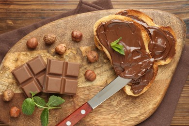 Photo of Toasts with tasty chocolate spread, pieces, mint and hazelnuts on wooden table, top view