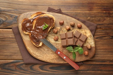 Photo of Toasts with tasty chocolate spread, pieces, mint and hazelnuts on wooden table, top view