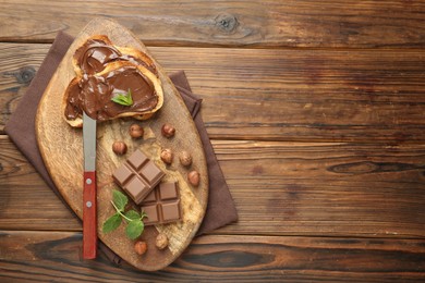 Photo of Toasts with tasty chocolate spread, pieces, mint and hazelnuts on wooden table, top view. Space for text
