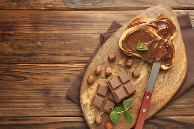 Photo of Toasts with tasty chocolate spread, pieces, mint and hazelnuts on wooden table, top view. Space for text