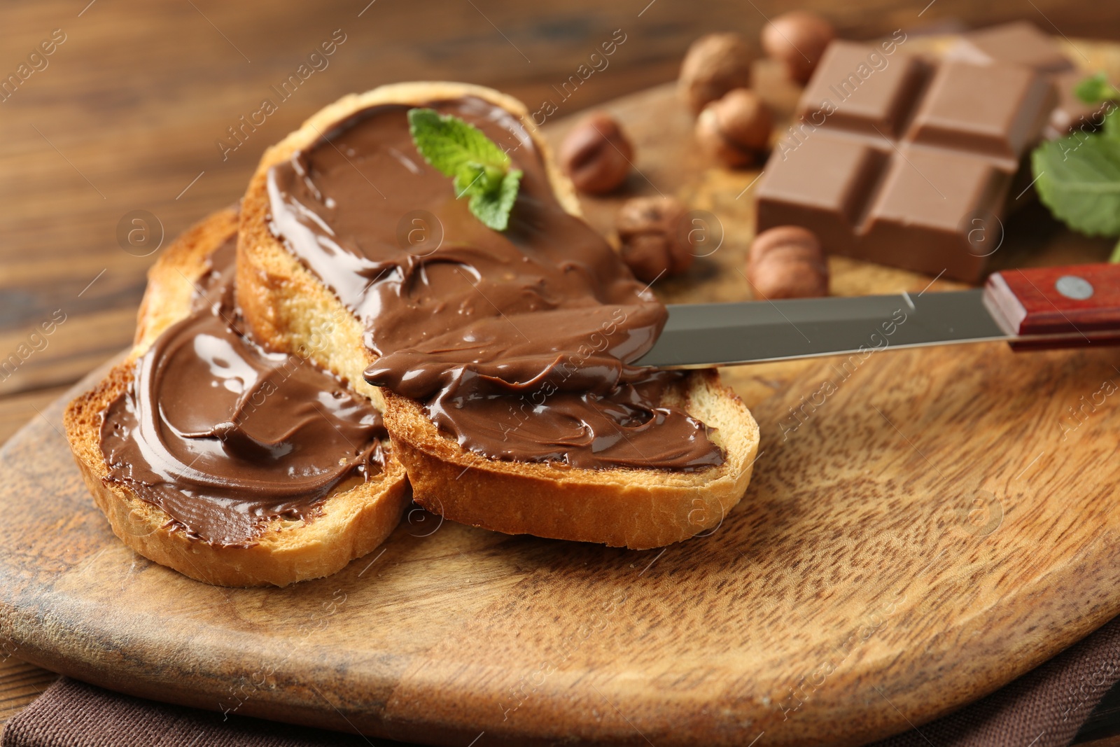Photo of Toasts with tasty chocolate spread, pieces, mint and hazelnuts on table, closeup