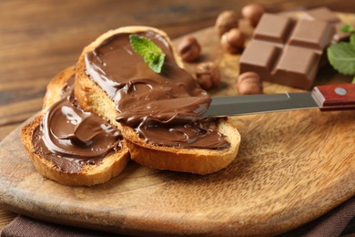 Photo of Toasts with tasty chocolate spread, pieces, mint and hazelnuts on table, closeup