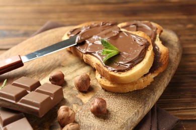 Photo of Toasts with tasty chocolate spread, pieces, mint and hazelnuts on table, closeup