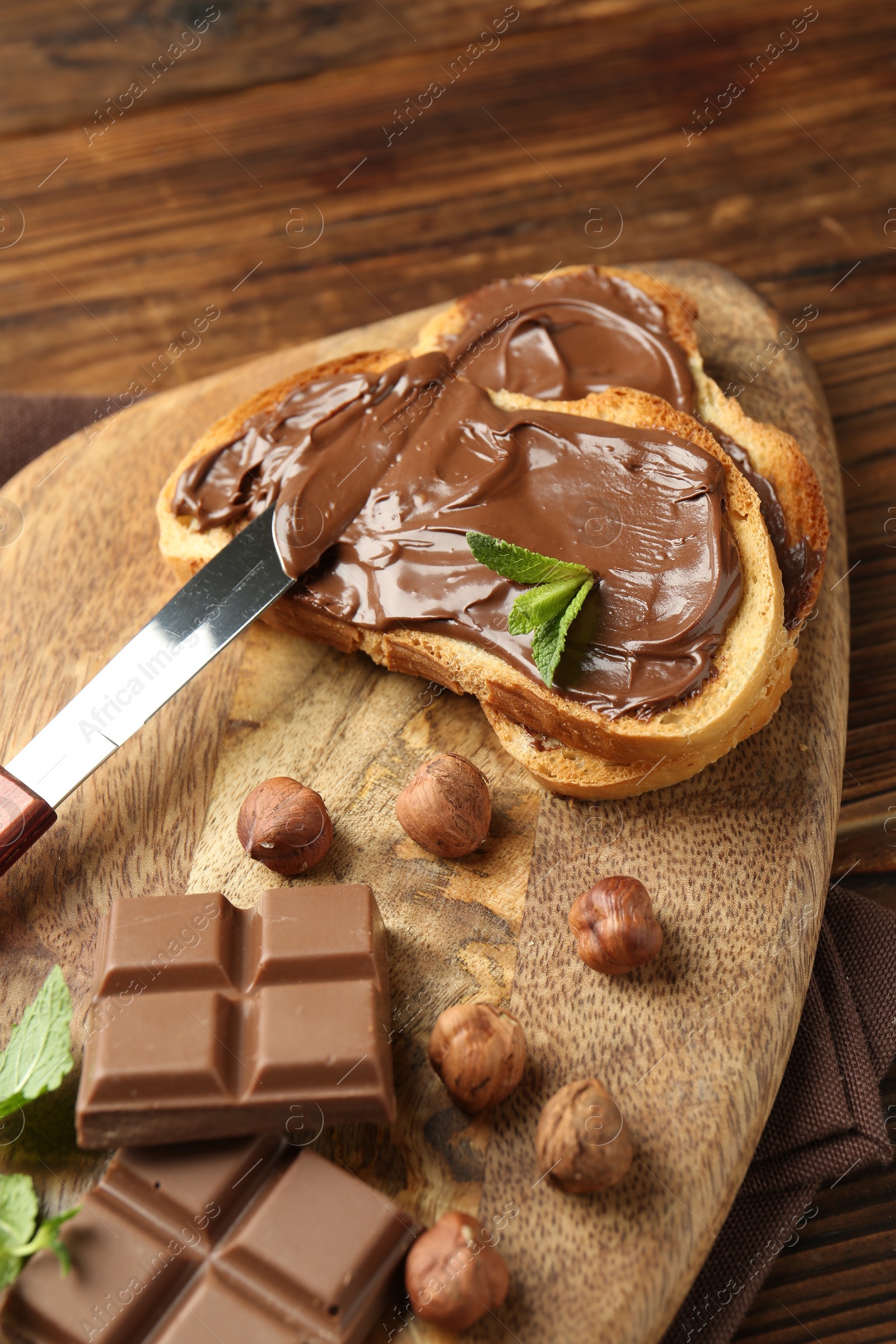 Toasts with tasty chocolate spread, pieces, mint and hazelnuts on wooden table, closeup Photo of Toasts with tasty chocolate spread, pieces, mint and hazelnuts on wooden table, closeup