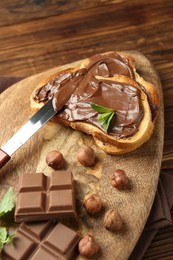 Photo of Toasts with tasty chocolate spread, pieces, mint and hazelnuts on wooden table, closeup