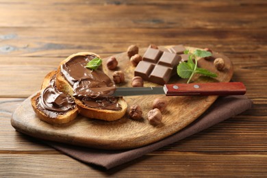 Photo of Toasts with tasty chocolate spread, pieces, mint and hazelnuts on wooden table, closeup
