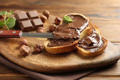 Photo of Toasts with tasty chocolate spread, pieces, mint and hazelnuts on wooden table, closeup