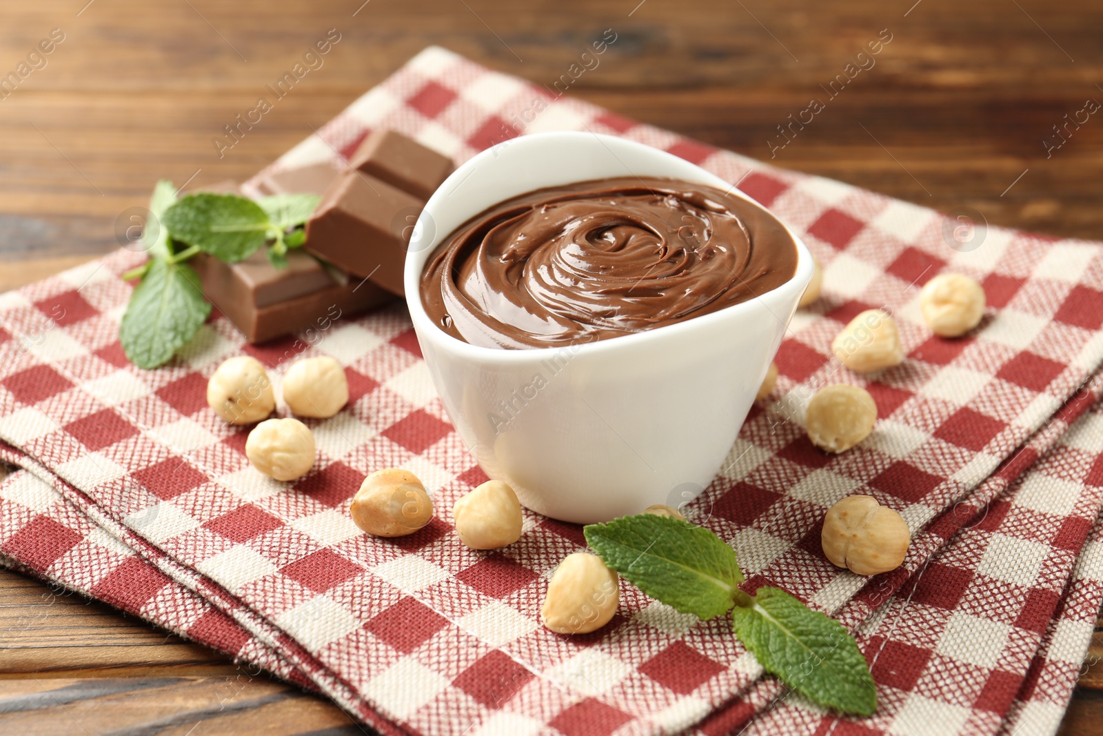 Tasty chocolate spread, pieces, mint and hazelnuts on wooden table, closeup Photo of Tasty chocolate spread, pieces, mint and hazelnuts on wooden table, closeup