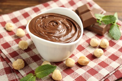 Photo of Tasty chocolate spread, pieces, mint and hazelnuts on table, closeup