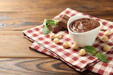 Photo of Tasty chocolate spread, pieces, mint and hazelnuts on wooden table, closeup. Space for text
