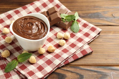 Photo of Tasty chocolate spread, pieces, mint and hazelnuts on wooden table, closeup