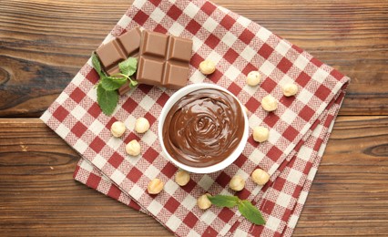 Photo of Tasty chocolate spread, pieces, mint and hazelnuts on wooden table, flat lay