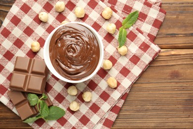 Photo of Tasty chocolate spread, pieces, mint and hazelnuts on wooden table, flat lay