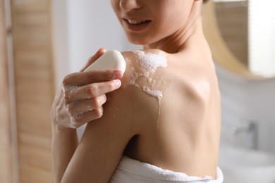 Photo of Woman washing body with soap bar indoors, closeup