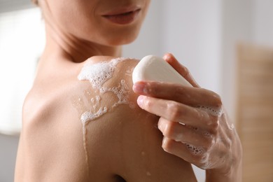 Photo of Woman washing body with soap bar indoors, closeup