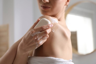 Photo of Woman washing body with soap bar indoors, closeup