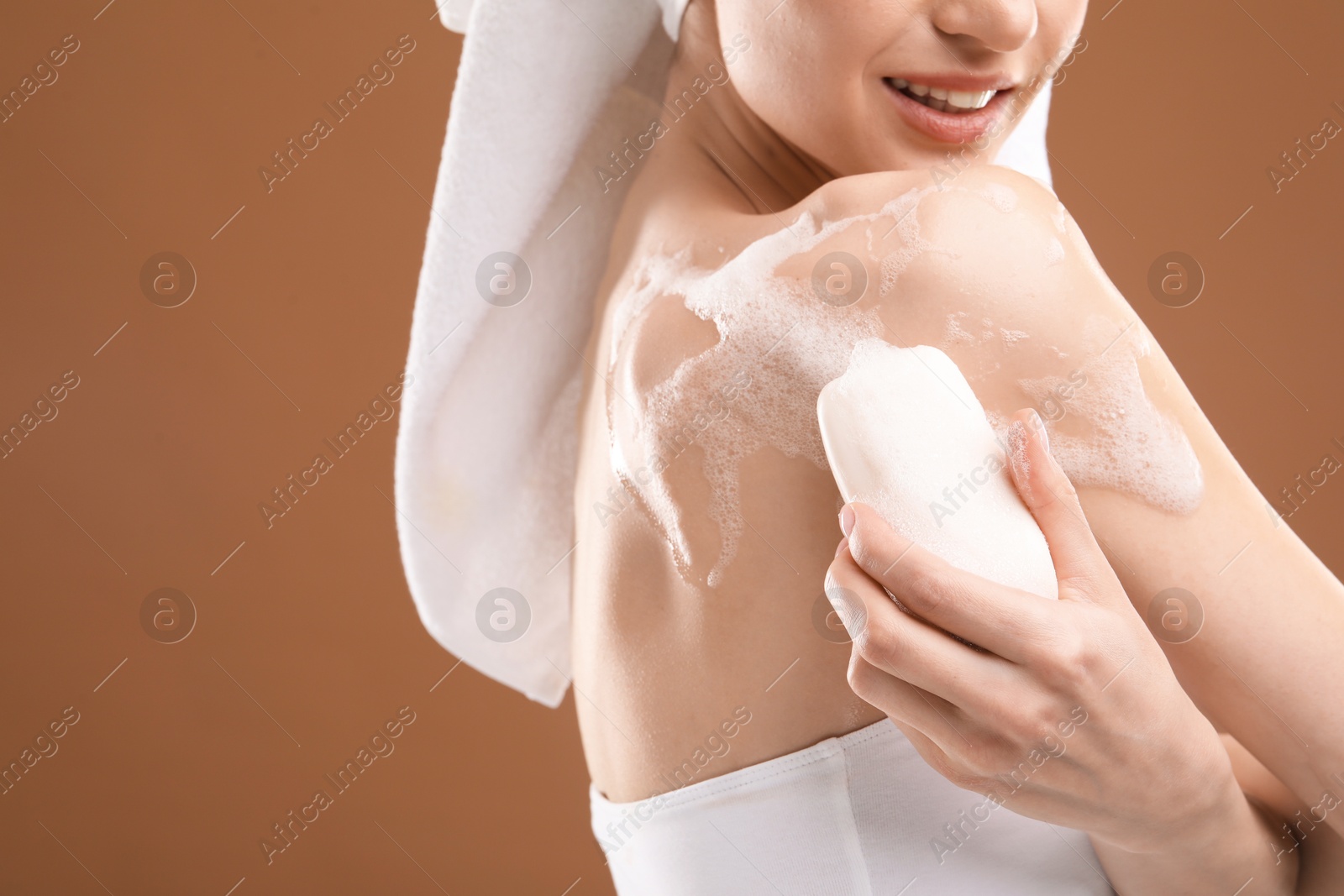 Smiling woman washing body with soap bar on brown background, closeup. Space for text Photo of Smiling woman washing body with soap bar on brown background, closeup. Space for text