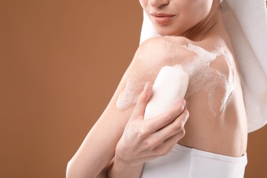 Photo of Woman washing body with soap bar on brown background, closeup. Space for text