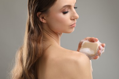 Photo of Beautiful woman washing body with soap bar on grey background, closeup