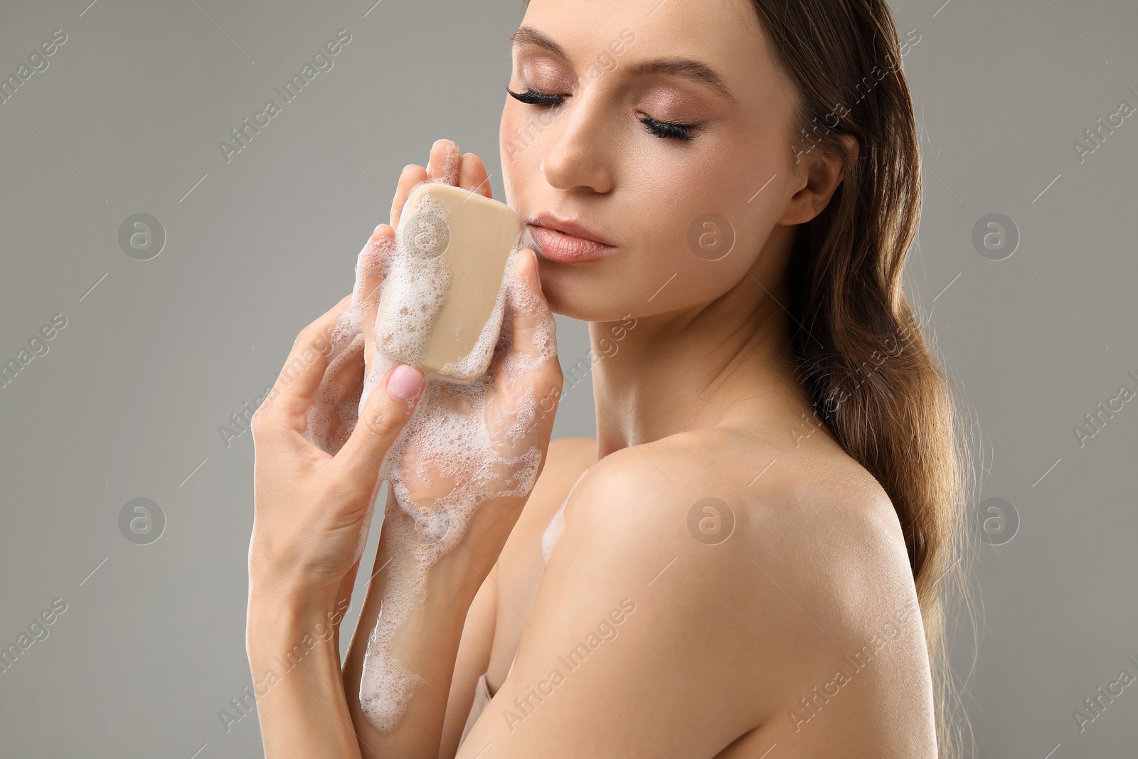 Beautiful woman with soap bar on grey background, closeup Photo of Beautiful woman with soap bar on grey background, closeup