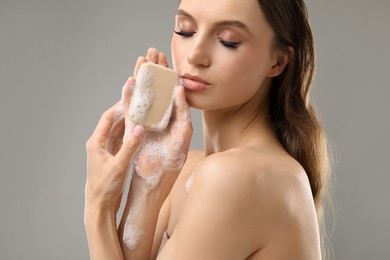Photo of Beautiful woman with soap bar on grey background, closeup