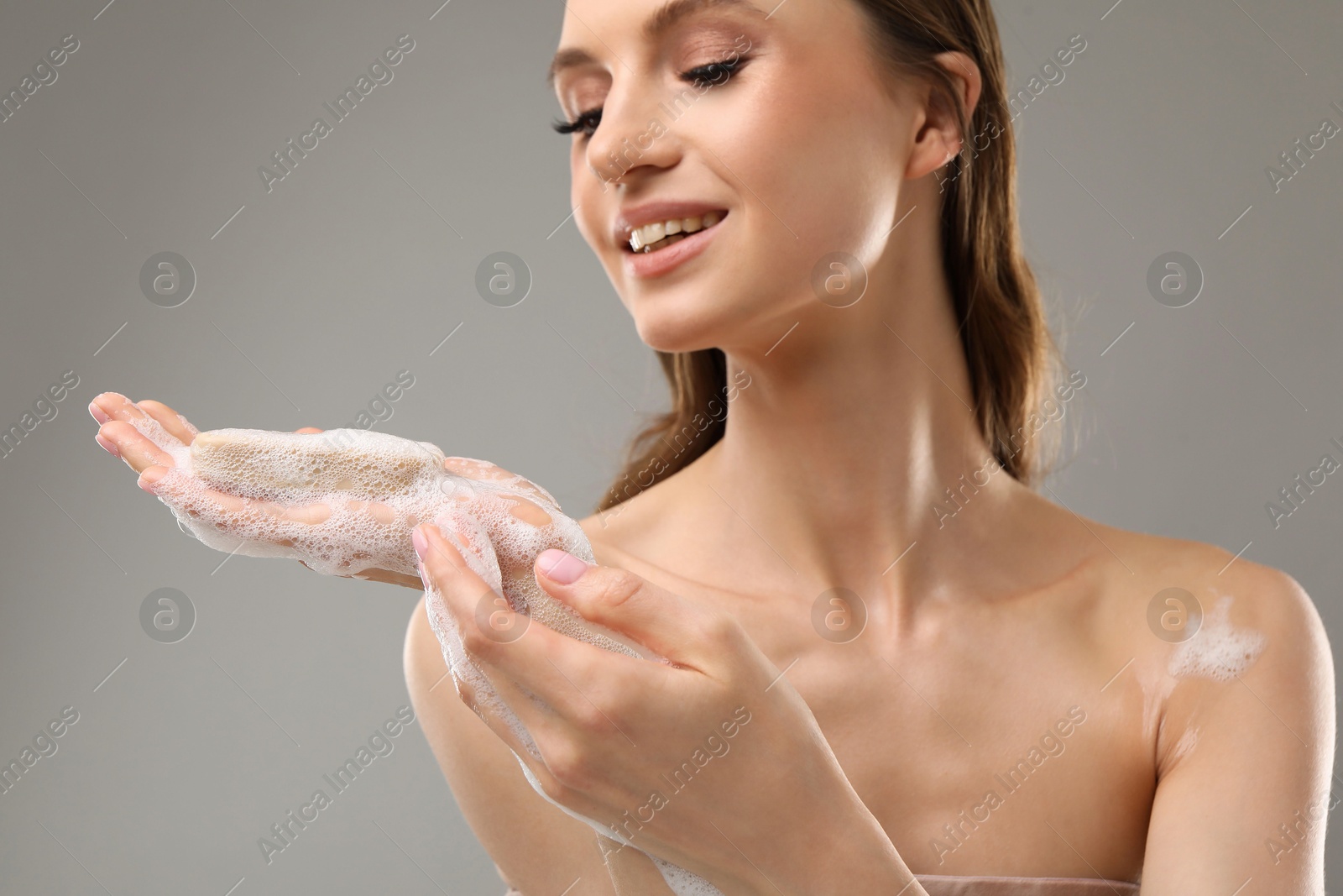 Smiling woman with soap bar on grey background, closeup Photo of Smiling woman with soap bar on grey background, closeup