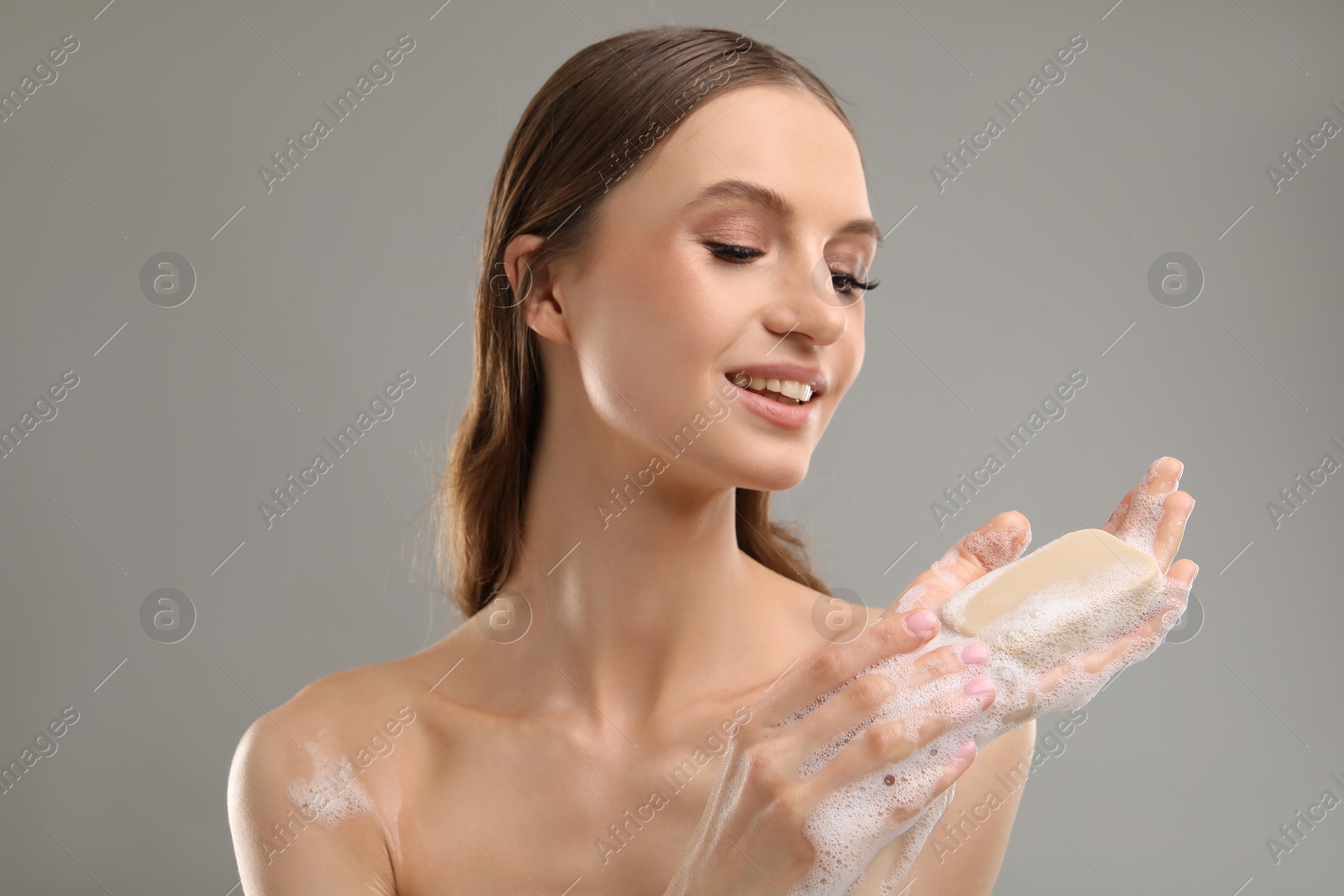 Smiling woman with soap bar on grey background, closeup Photo of Smiling woman with soap bar on grey background, closeup