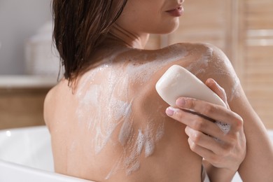 Photo of Woman washing body with soap bar in bathroom, closeup