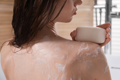 Photo of Woman washing body with soap bar in bathroom, closeup