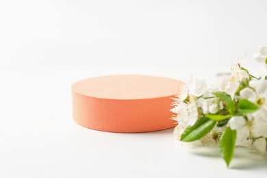 Photo of Round podium and twig with beautiful flowers on white background, closeup. Space for text