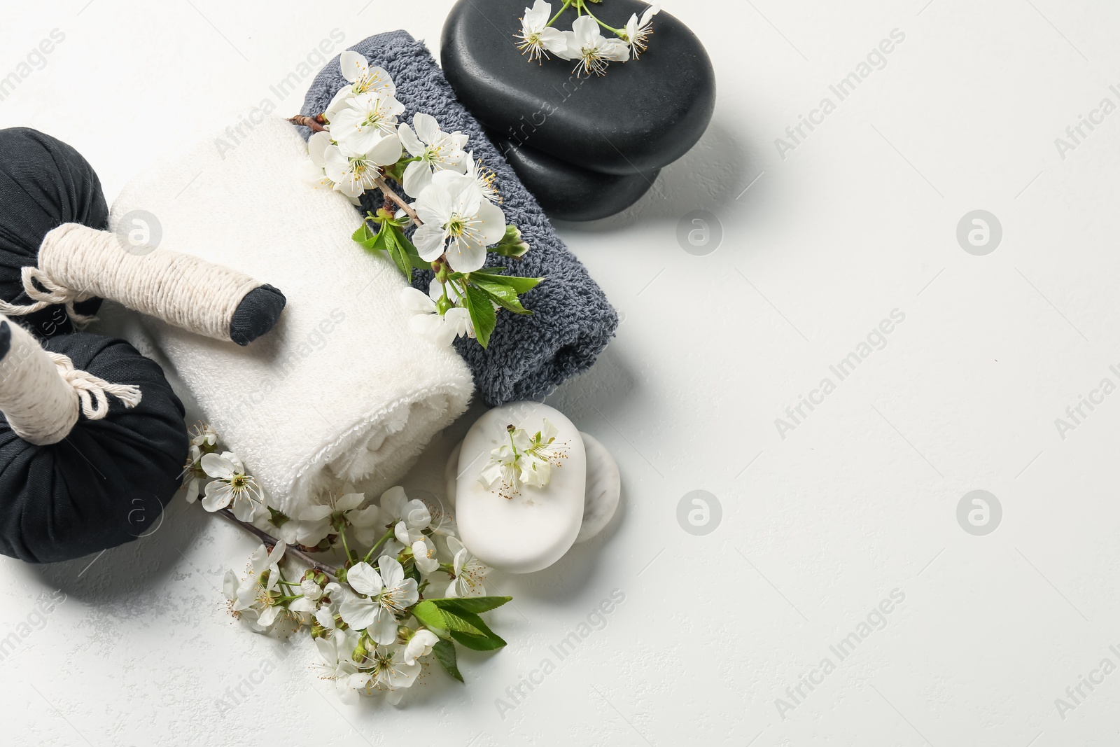Spa composition with pebble stones, beautiful flowers and herbal bags on white textured table, flat lay. Space for text Photo of Spa composition with pebble stones, beautiful flowers and herbal bags on white textured table, flat lay. Space for text