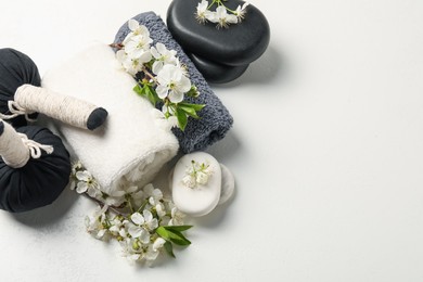 Photo of Spa composition with pebble stones, beautiful flowers and herbal bags on white textured table, flat lay. Space for text
