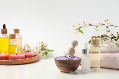 Photo of Composition with spa products, beautiful flowers and burning candles on white table, closeup