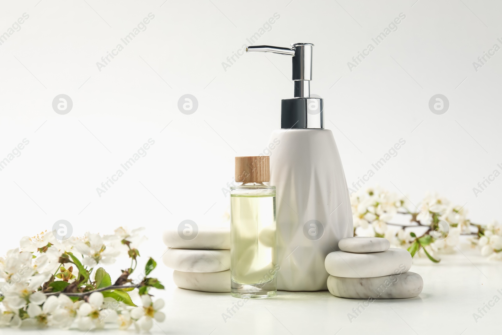 Spa products, pebble stones and twigs with beautiful flowers on white table, closeup Photo of Spa products, pebble stones and twigs with beautiful flowers on white table, closeup